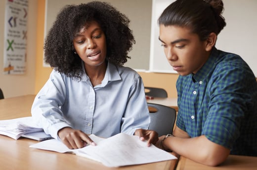 high-school-tutor-giving-male-student-one-to-one-tuition-at-desk